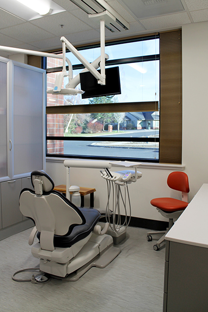 A treatment room set in front of a large window looking out to the neighborhood, a tv hangs from the ceiling